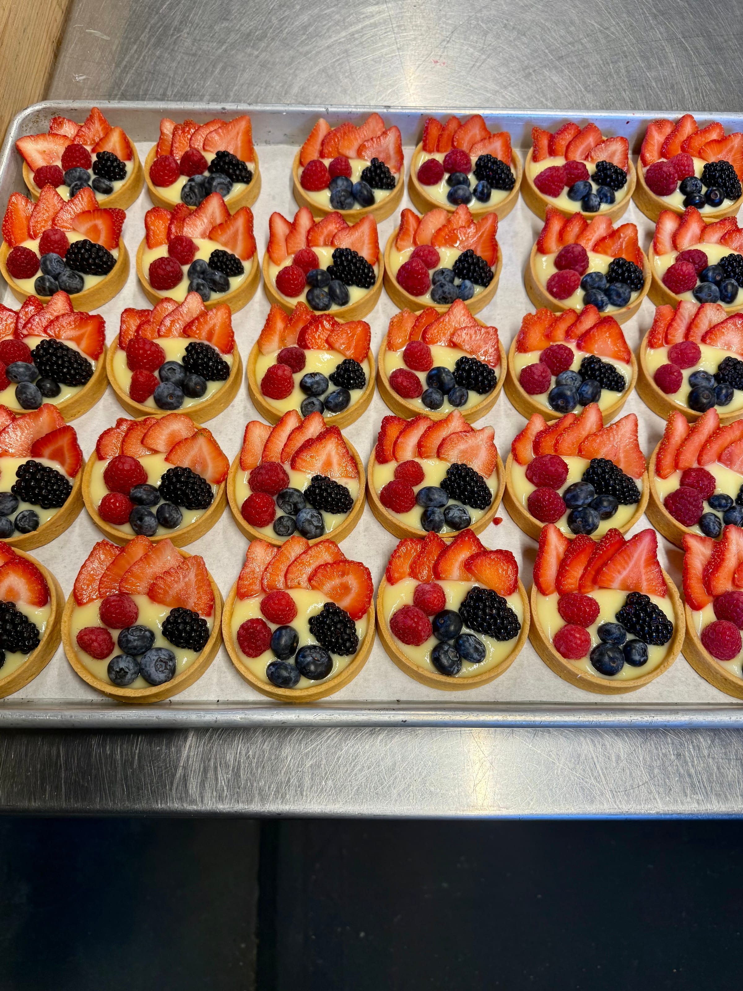 A tray of Maya Papaya's handmade fruit tarts topped with strawberries, blueberries, blackberries, and raspberries